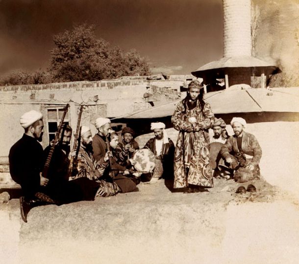 Deček, oblečen v pražnja ženska oblačila, navdihuje moške v Samarkandu (Uzbekistan). Fotografija je bila posneta približno med letoma 1905 in 1915 (avtor je Prokudin Gorski, fotografijo pa hrani kongresna knjižnica v Washingtonu)