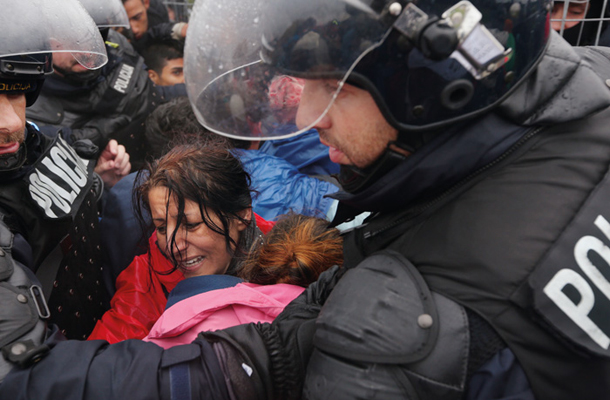 Ponedeljek zjutraj, Središče ob Dravi. Policisti spuščajo begunce z območja med državama proti Sloveniji. Na sliki je mati z otrokom, ki jo je množica stisnila. Pristopita policista in jo zavarujeta pred pritiskom.